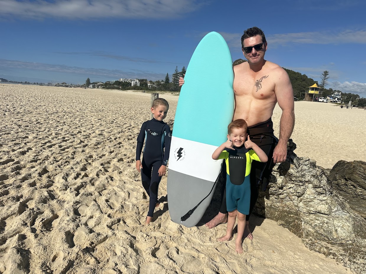 Byron and his sons at the beach with a surfboard.